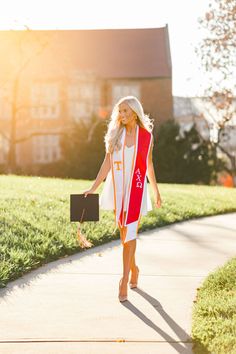 a woman in a red and white graduation gown walking down a sidewalk with her diploma