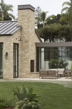 a stone house with glass doors and a bench in the front yard, surrounded by greenery