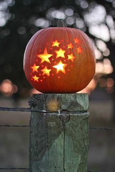 a carved pumpkin sitting on top of a wooden post with stars in the center,