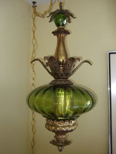 a green glass vase is hanging from a chain on the wall next to a mirror