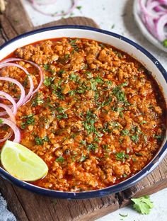 a bowl filled with chili and onions on top of a wooden cutting board next to sliced onion