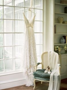 a dress hanging on a hanger next to a chair in front of a window