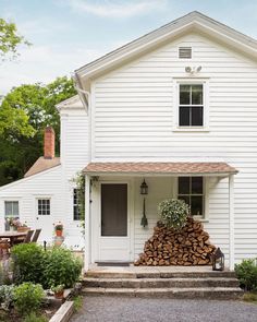 a white house with stacked firewood in the front yard and steps leading up to it