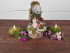 an arrangement of flowers and plants in a basket on top of a wooden table with candles