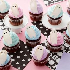 cupcakes decorated with icing and ghost decorations on plates, sitting on a table