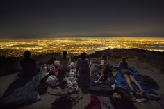 people sitting on top of a hill at night with the city lights in the background