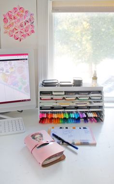 a desk with a computer, notebook and crayons in front of the window