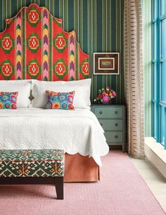 a bed with colorful headboard and pillows in a room that has green striped walls