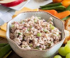 a bowl filled with tuna salad surrounded by grapes, celery and carrots