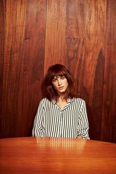 a woman sitting at a wooden table in front of a wood paneled wall with her hands on her hips