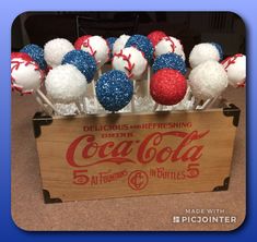 a wooden crate filled with red, white and blue cake pops in the shape of baseballs