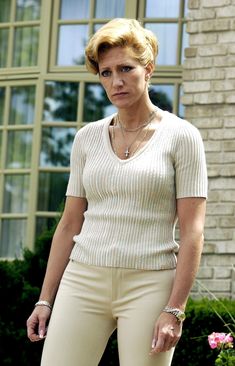 a woman standing in front of a brick building wearing white pants and a short sleeved sweater