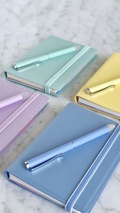 four different colored notebooks and a pen on a marble counter top with white background