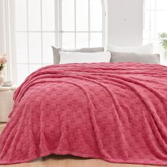 a bed covered in a pink blanket next to a window