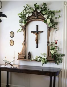 a cross is hanging on the wall next to a table with flowers and other decorations