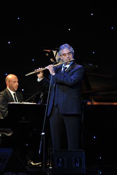 a man in a suit and tie plays the flute while another man stands behind him