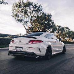 the rear end of a white sports car driving on a road with trees in the background