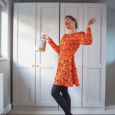 a woman in an orange polka dot dress holding a can