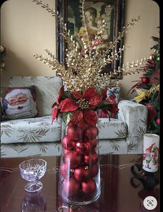 a glass vase filled with red balls and poinsettis on a coffee table