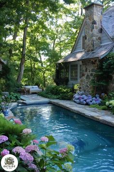 an outdoor swimming pool surrounded by flowers and greenery with a stone house in the background