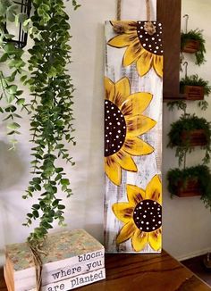 a wooden sign with sunflowers on it next to a box and some potted plants