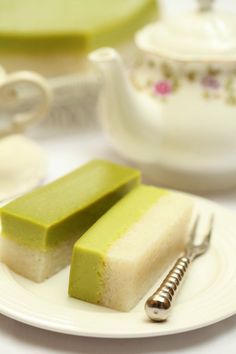 two pieces of cake on a plate with a tea pot in the back ground and other dishes