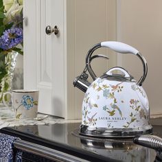 a white tea kettle sitting on top of a stove next to a vase with flowers