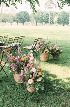 an outdoor setting with chairs and flowers in baskets on the grass, surrounded by trees