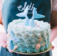 a person holding a cake with blue icing and two fish on it's side