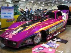 a purple car is parked in a garage with other cars and people looking at it