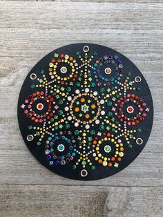 a black plate with multicolored beads on it sitting on a wooden table next to a pair of scissors