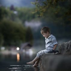 a young boy sitting on the edge of a body of water