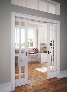 an open door leading to a kitchen and dining room with white walls, hardwood flooring and windows