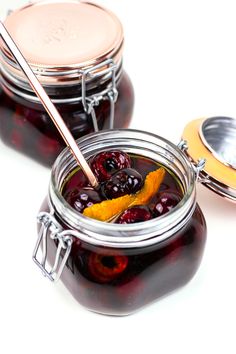 two jars filled with jam and orange peels next to a spoon on a white surface