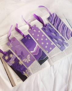 four bookmarks with purple and white designs are laying on top of an open book