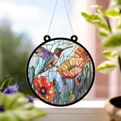 a stained glass hummingbird hanging on a window sill with flowers in the background