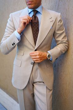 a man in a white suit adjusting his green neck tie and looking at the camera