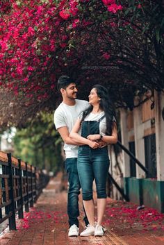 a man and woman standing next to each other in front of trees with pink flowers