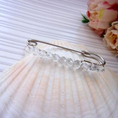 a close up of a hair pin on a sea shell with flowers in the background