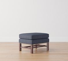 a square footstool sitting on top of a hard wood floor next to a white wall