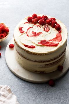 a cake with white frosting and raspberries on top sitting on a plate