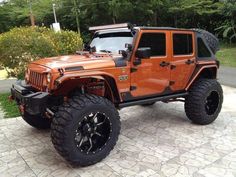 an orange jeep is parked in front of some bushes