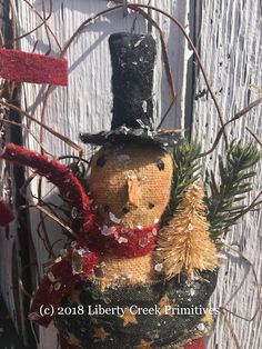 a snowman ornament is hanging on a fence with branches and pine cones