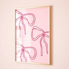 a pink and gold framed art piece with bows on it's side against a wall