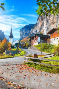 an empty road in the mountains with houses and trees on both sides, surrounded by fall foliage