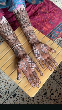 the hands and feet of a woman with henna tattoos on their arms, sitting on a bamboo mat