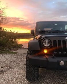 a black jeep parked on the side of a road near a body of water at sunset