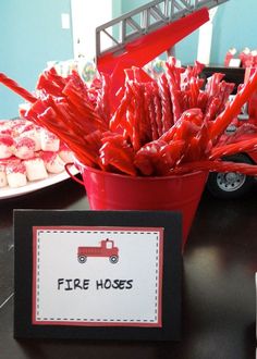 a red bucket filled with candy sitting on top of a table next to a sign that says fire hoses