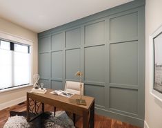 a desk in the corner of a room with blue paneled walls and wooden floors