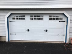 two white garage doors with windows on the side of a gray and white building next to potted plants